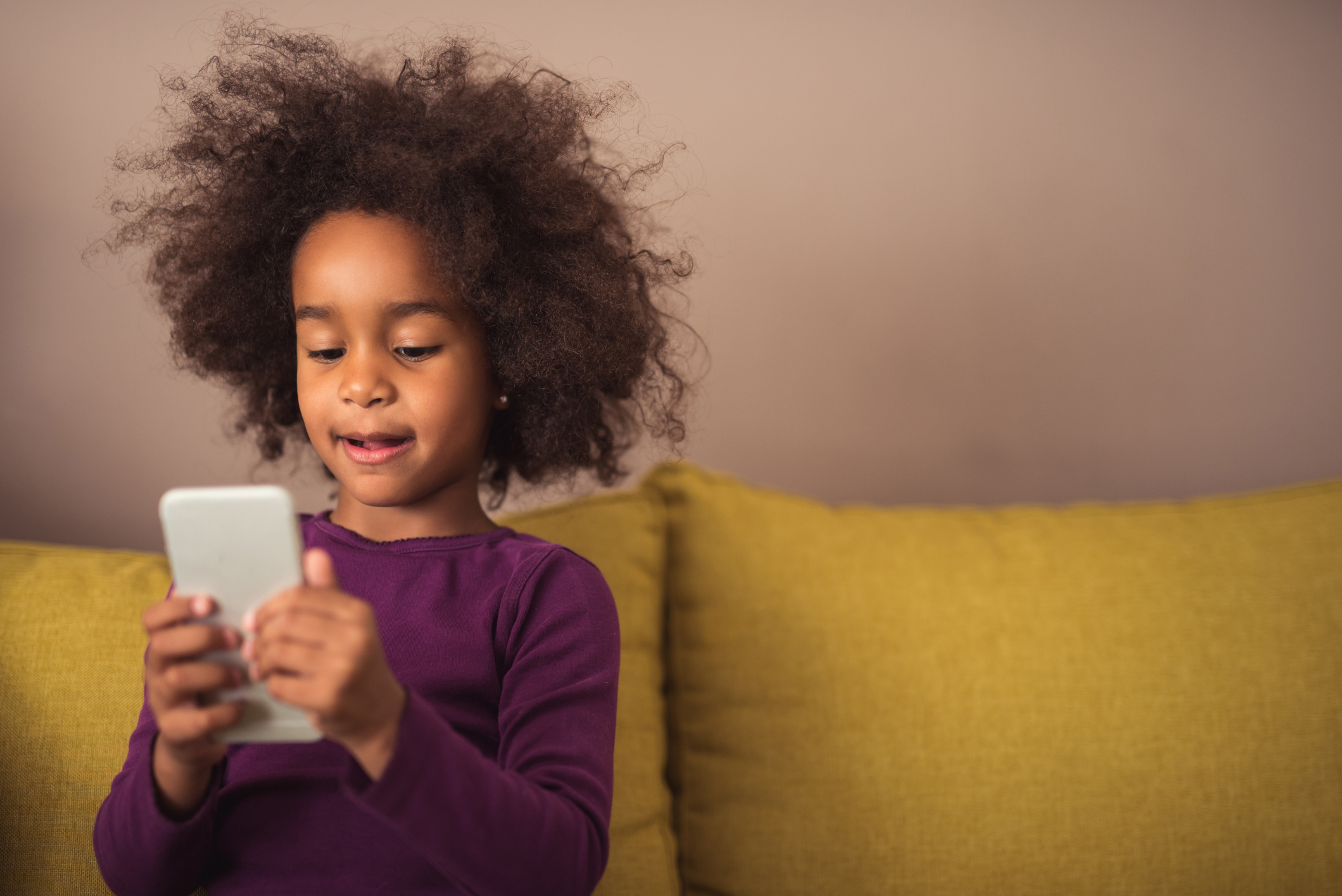 A child sitting on a sofa using a mobile phone