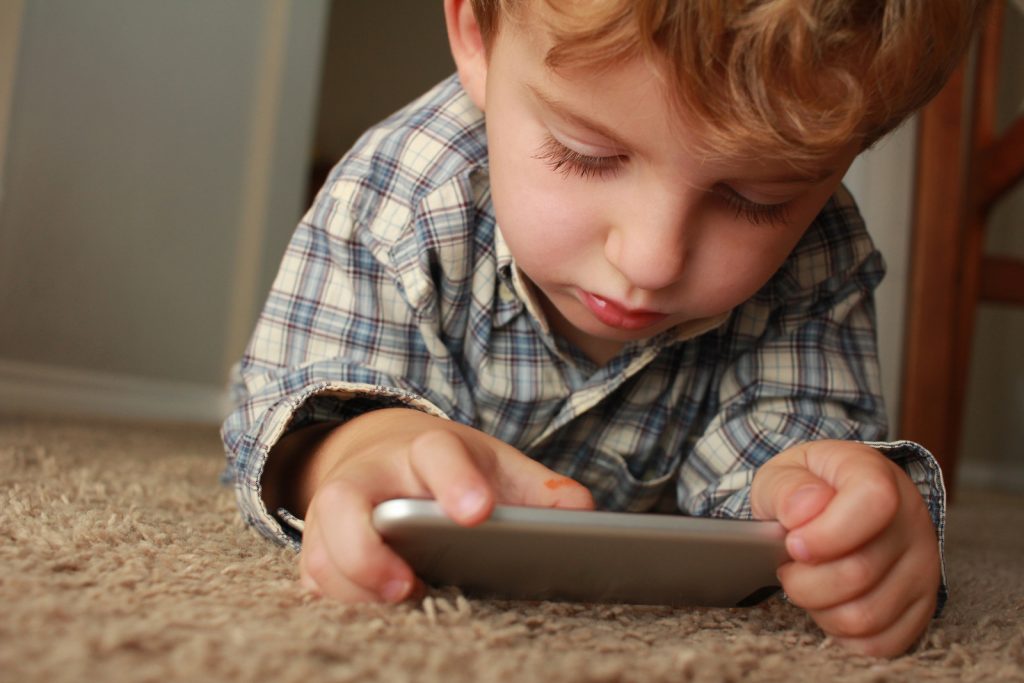 A child laying on the floor playing on a mobile phone