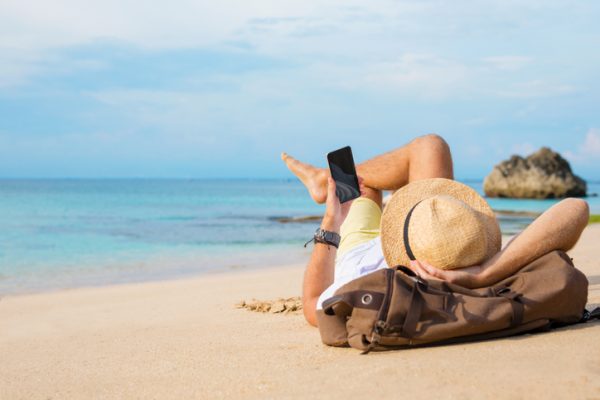 A man laying on a sandy beach using his mobile phone