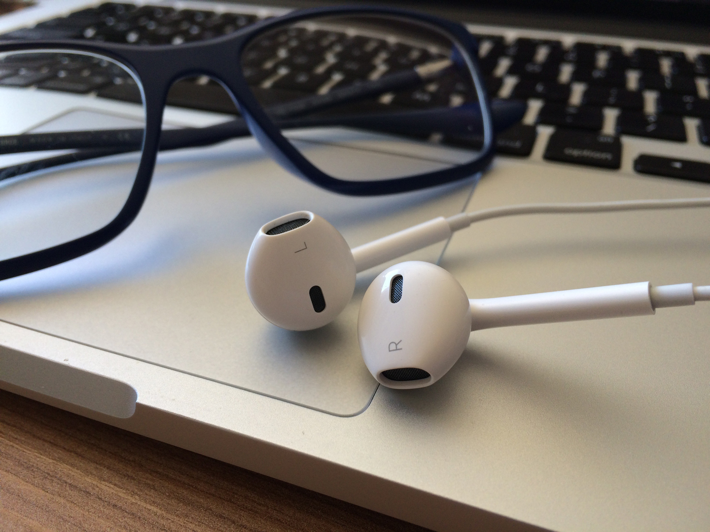 A pair of headphones resting on a laptop next to a pair of reading glasses