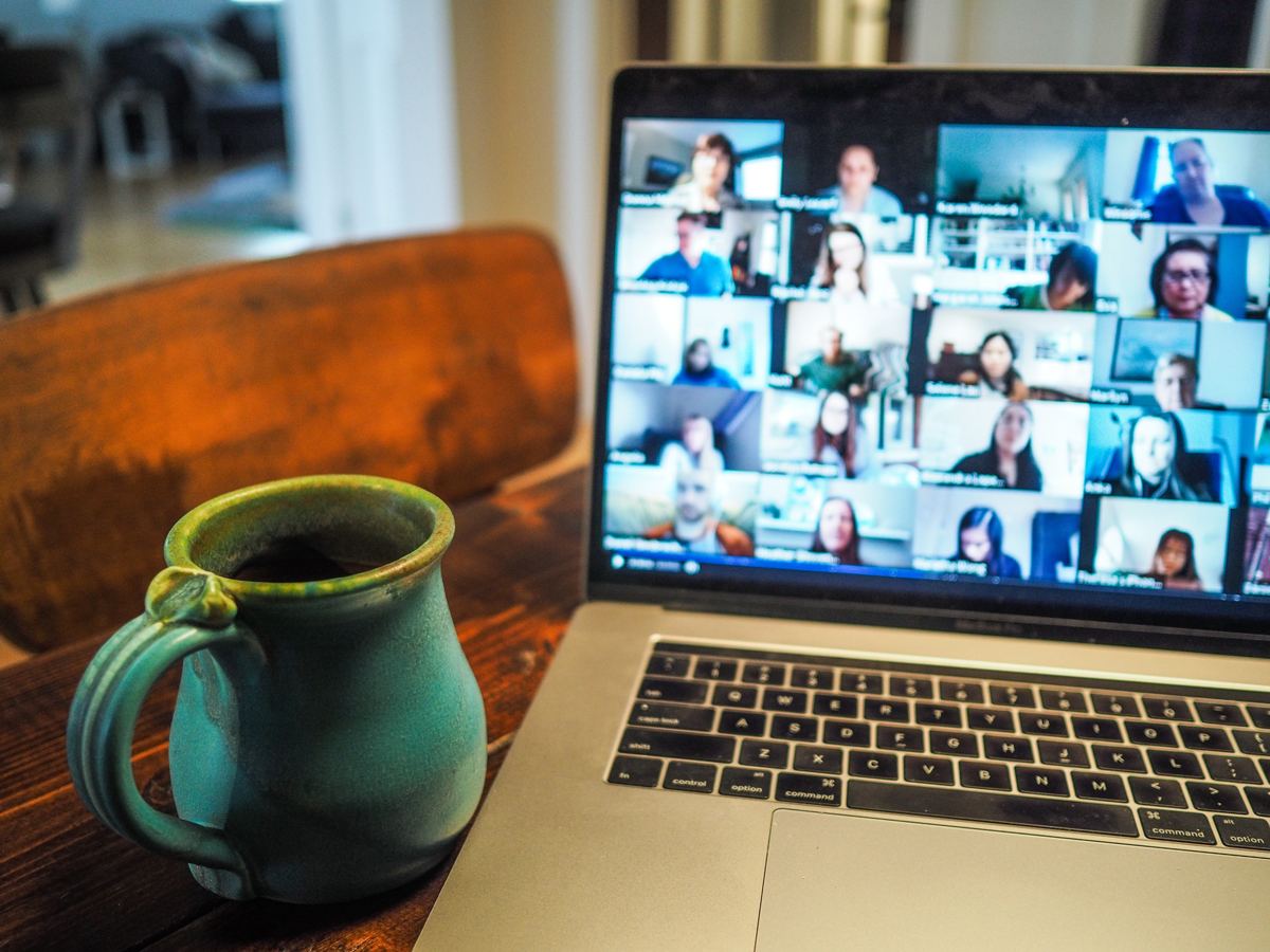 A laptop with a Zoom meeting taking place on screen with a mug of coffee next to it