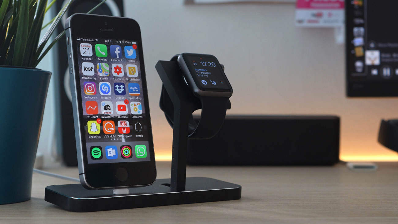 An iPhone and iWatch placed on a stand on a desk