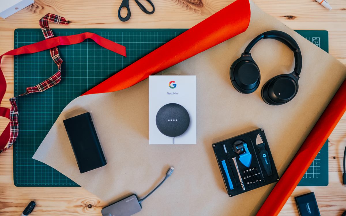 A Google Nest Mini on a table about to be wrapped in wrapping paper with other gadget gifts