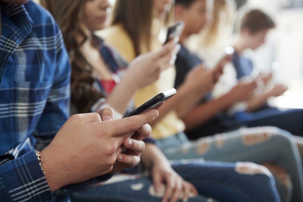 A line of young people siting in a row using their mobile phones