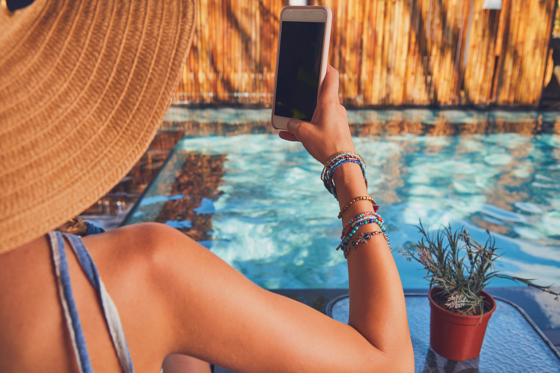 A woman in a large sun hat taking a picture on her mobile phone whilst on holiday