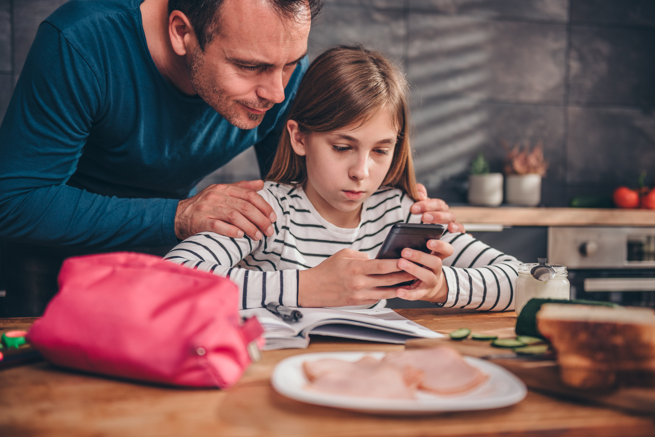 A parent leaning over their child observing them on a mobile phone