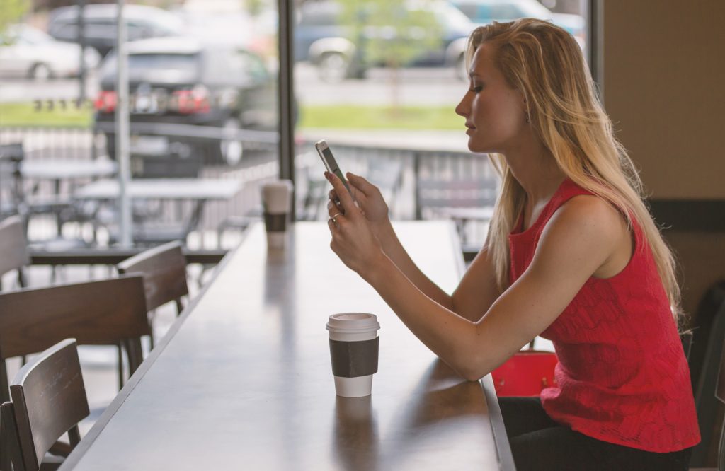 A woman sitting in a cafe on her own using her phone while having a coffee