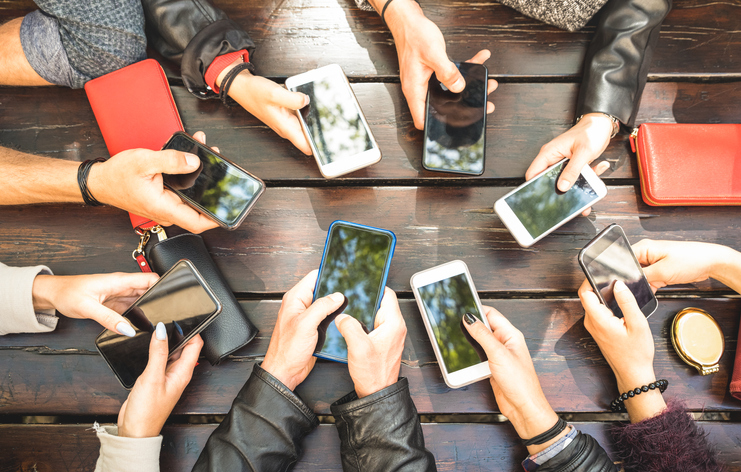 A group of people sitting around a table putting their mobile phones in making a circle