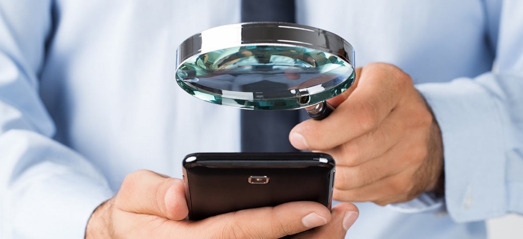 A man holding a magnifying glass over a mobile phone