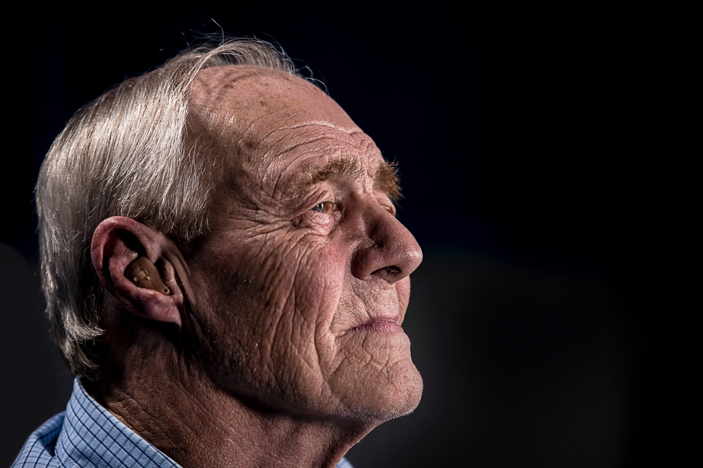 A smiling elderly person with a hearing aid in his ear