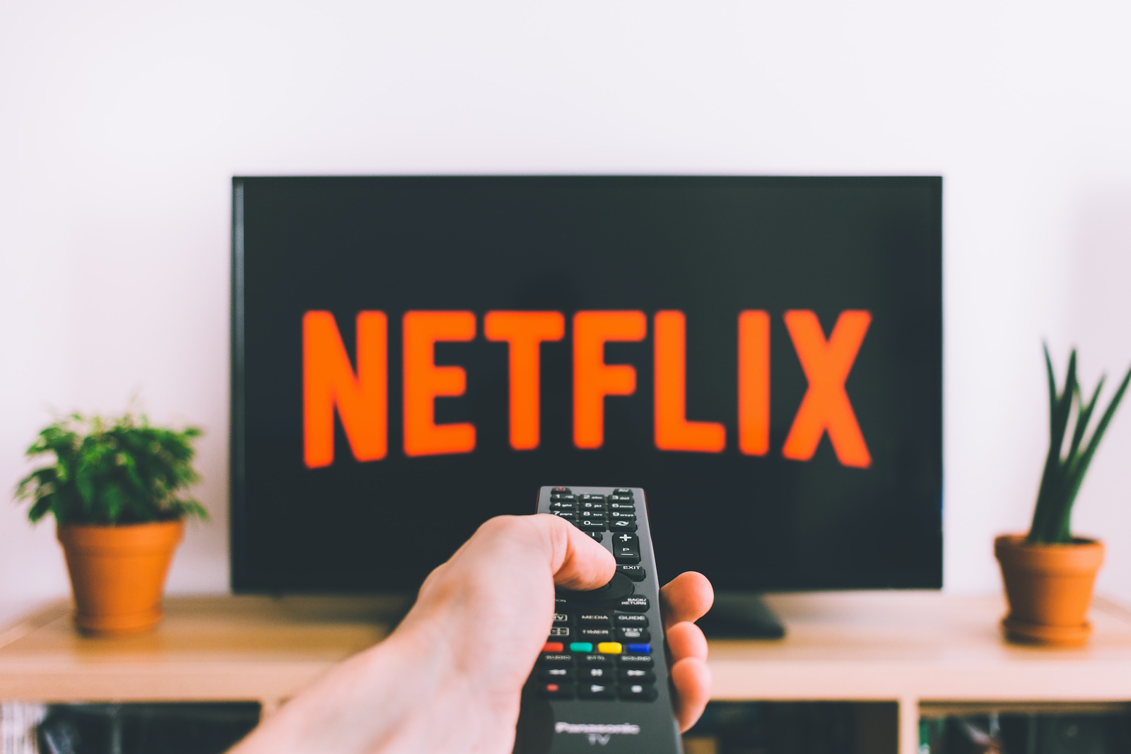 A person holding up a remote up to a TV displaying Netflix