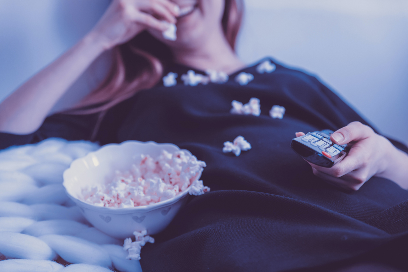 A women smiling s she eats popcorn while watching TV