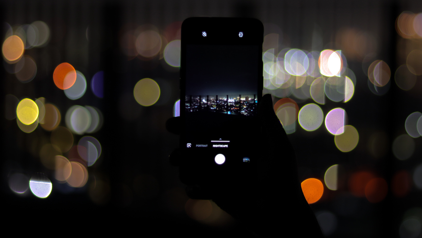 A OnePlus 8 Pro taking a picture at night with blurred city lights behind it