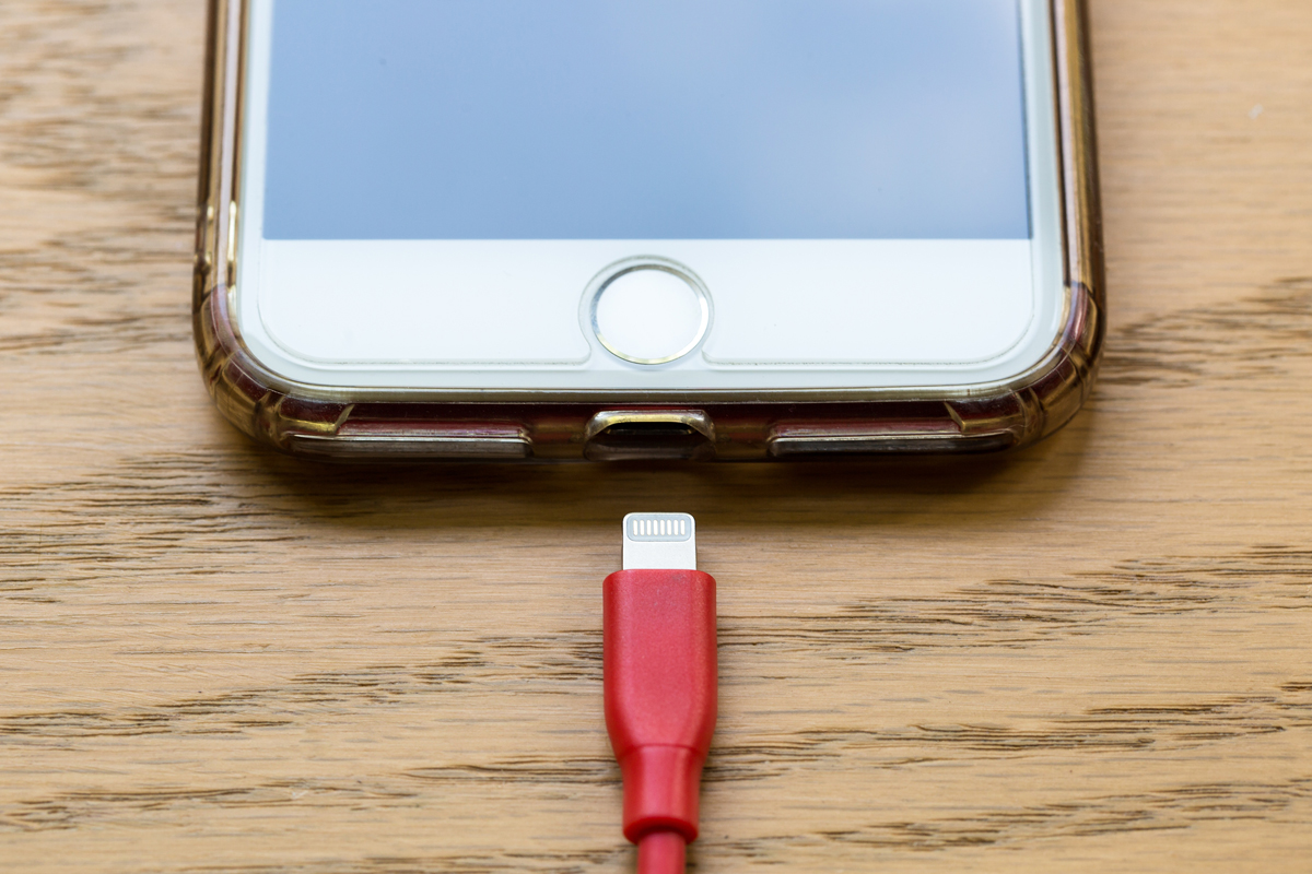 A red phone charger about to be plugged into an iPhone
