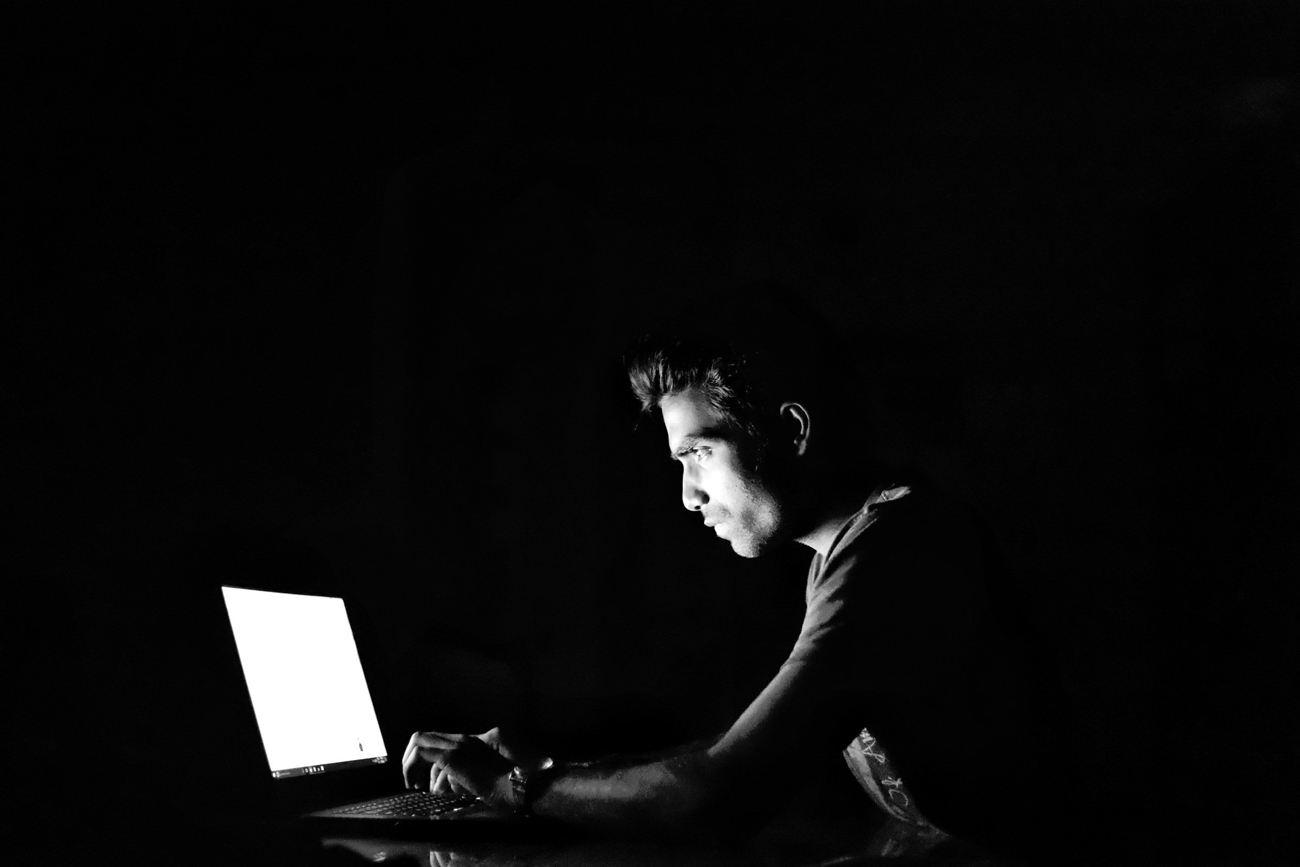 A man hacking on a laptop in a darkroom