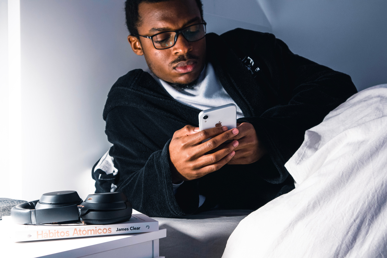 A man laying in bed getting ready to sleep using his iPhone with headphones next to his bedside