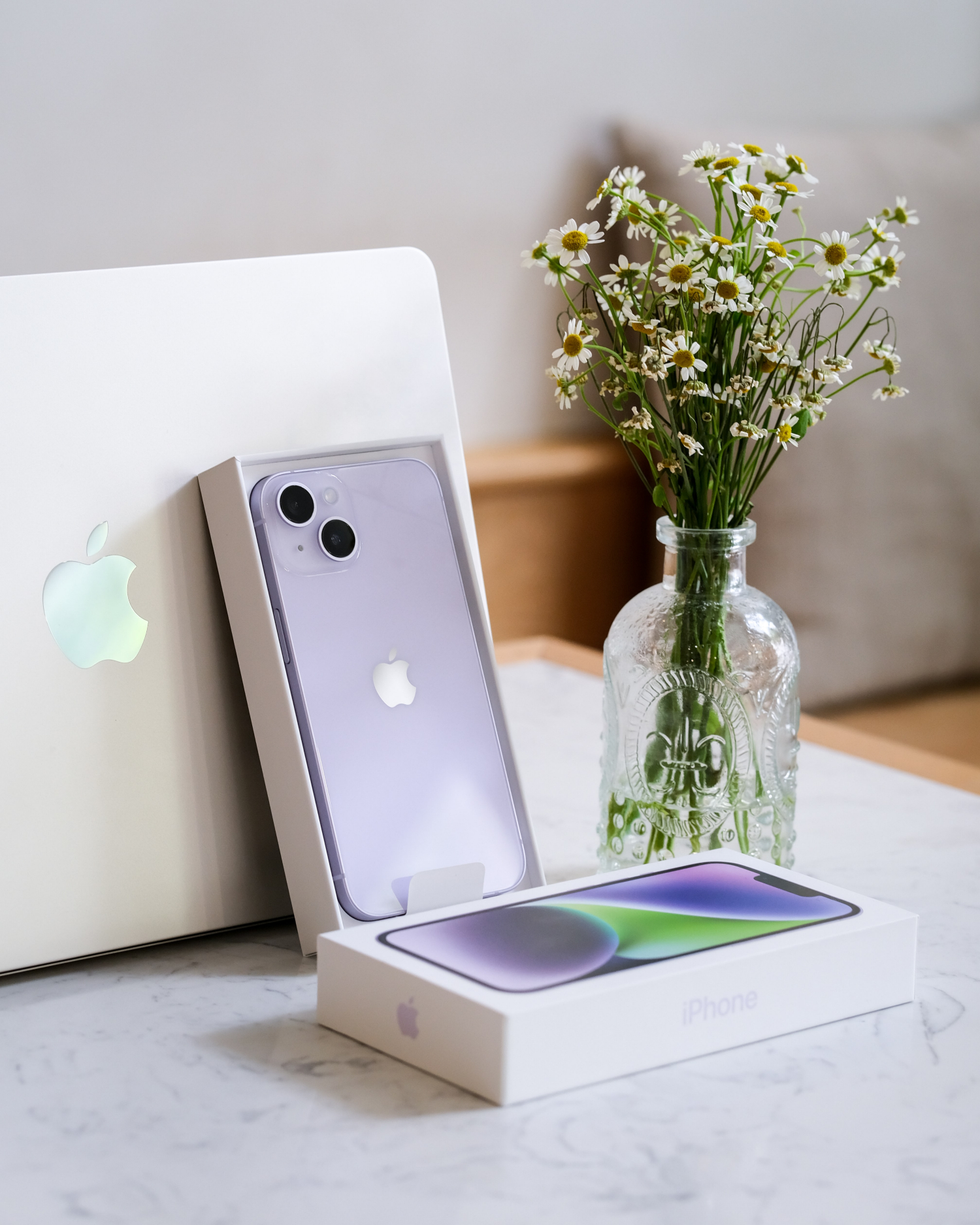 purple iphone 14 in its box placed against a macbook