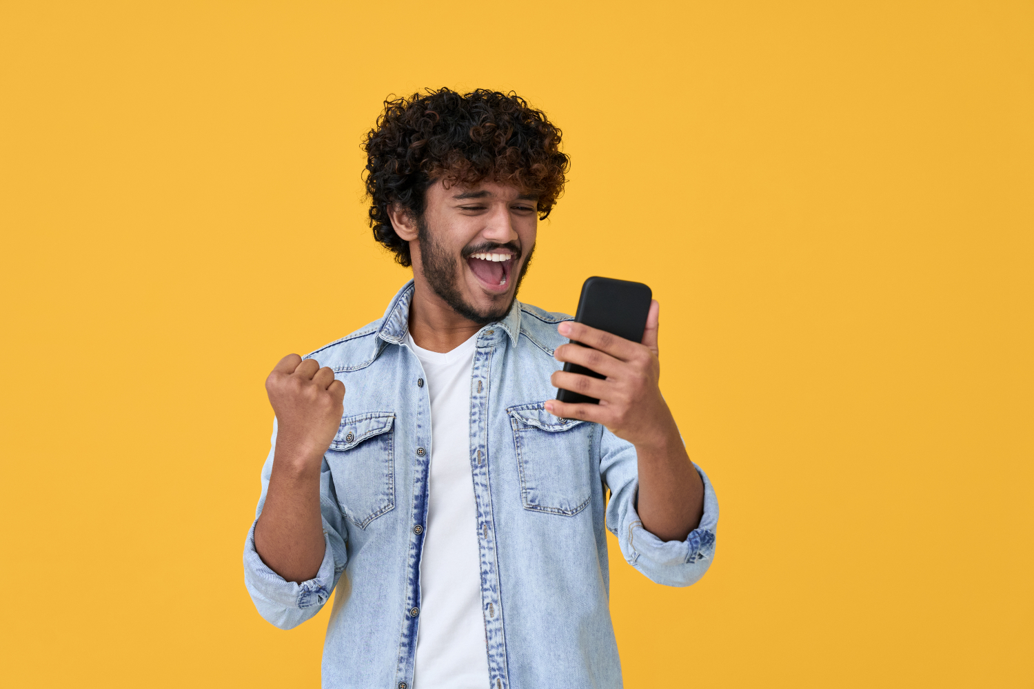 man cheering whilst holding a phone standing in front of a yellow background