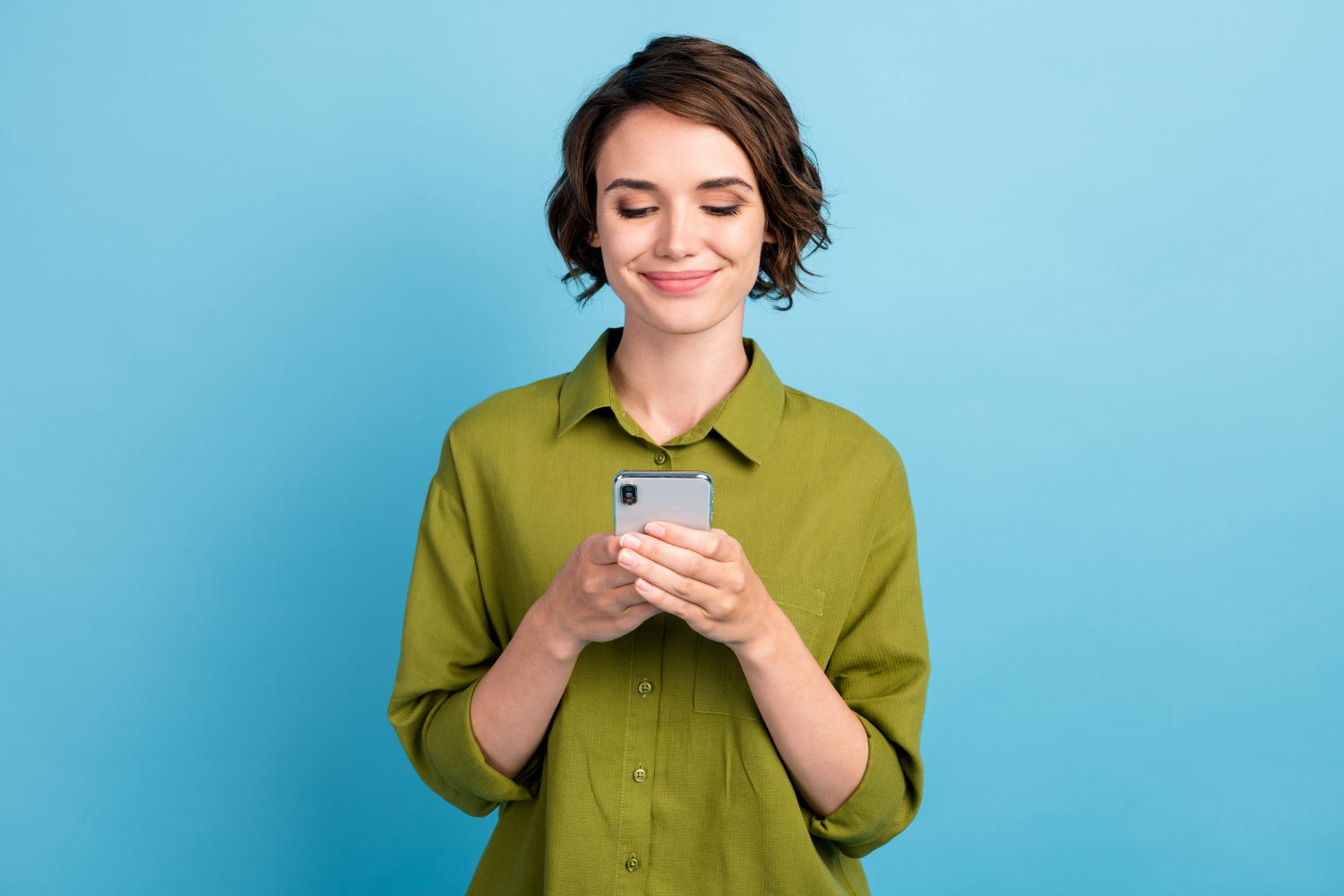 woman smiling whilst holding her phone in front of blue background